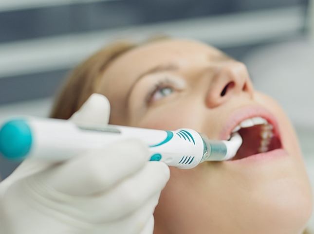 Woman having her teeth scanned by cavity detection system
