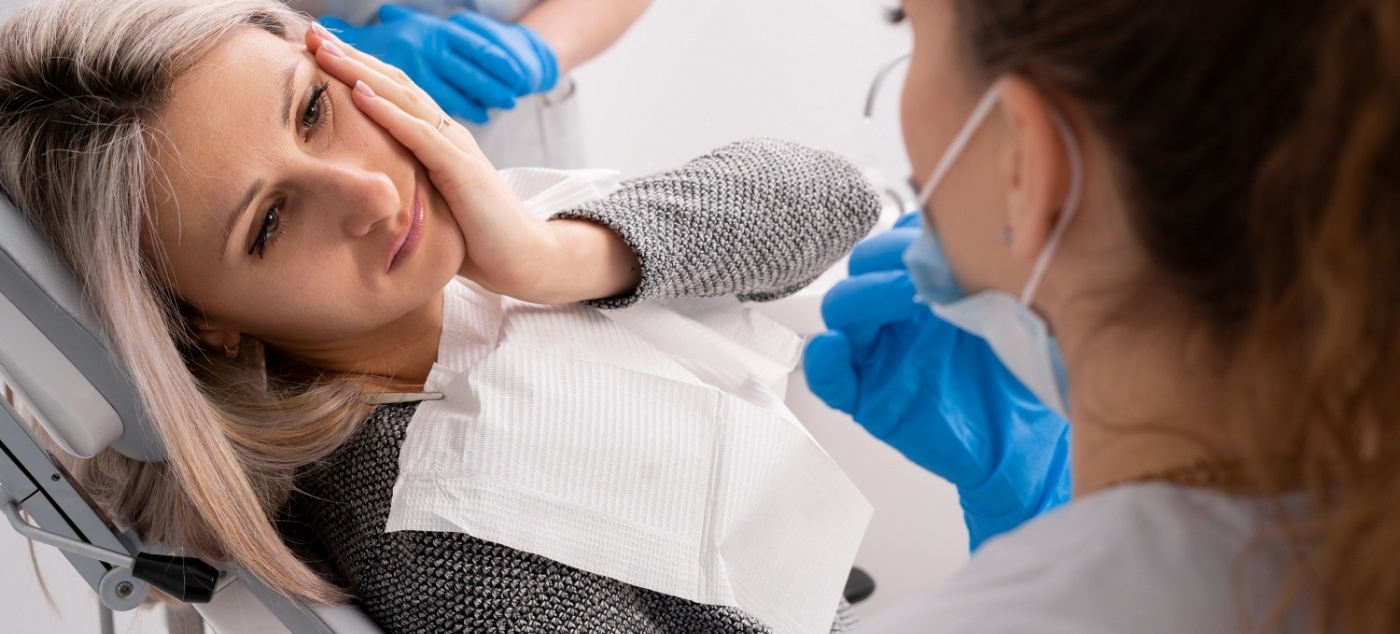 Woman in yellow sweater holding her jaw in pain needing emergency dentist