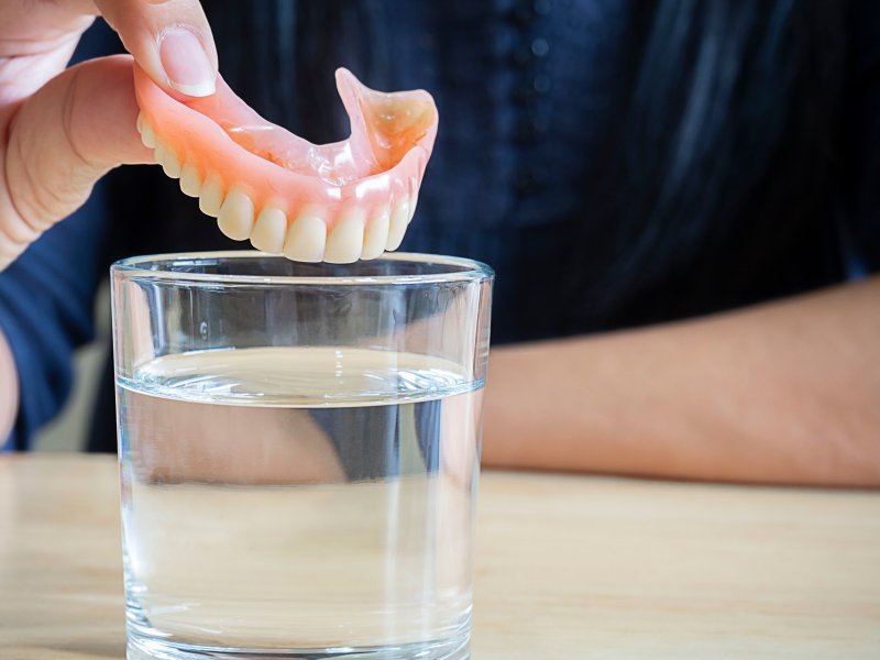 A person putting their dentures in a glass of solution